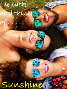 3 smiling people lying on the grass wearing sunglasses and looking up to the sky